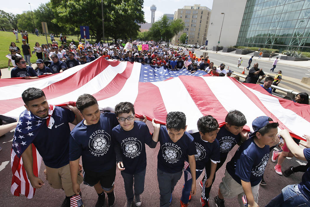 Jóvenes y adultos llevan una bandera americana durante una marcha de protesta por el centro de Dallas, el domingo 9 de abril de 2017. Miles de personas están marchando y reuniéndose en el centr ...