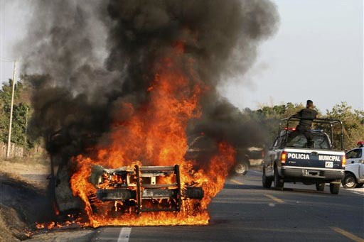 En esta foto de archivo se puede ver vehículo de la policía incendiándose, el 25 de febrero del 2009, en Zihuatanejo, México, mientras al lado pasa una camioneta de la policía. Ahora en un su ...