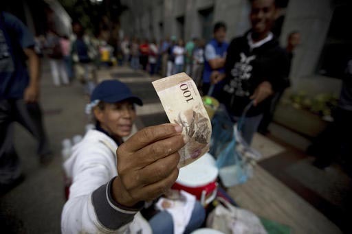 En Caracas, Venezuela, el martes 13 de diciembre del 2016, un vendedor de la calle inspecciona un billete de 100 bolívares mientras gente hace fila para cambiar sus billetes de esa denominación  ...