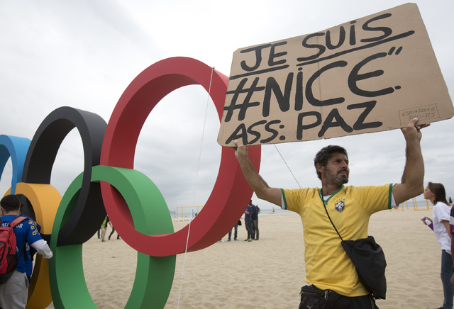 A man holds a sign to show solidarity with Nice during the presentation of Olympic rings made from recycled material, at Copacabana beach in Rio de Janeiro, Brazil, Thursday, July 21, 2016. Brazil ...