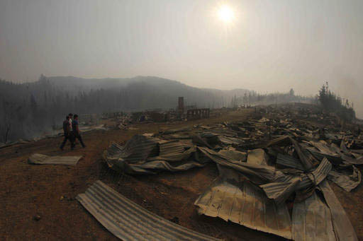 Unos hombres caminan cerca de los restos de casas arrasadas por el fuego, en Santa Olga, Chile, el jueves 26 de enero del 2017. Los 6,000 pobladores lograron escapar de lo que se considera el peor ...