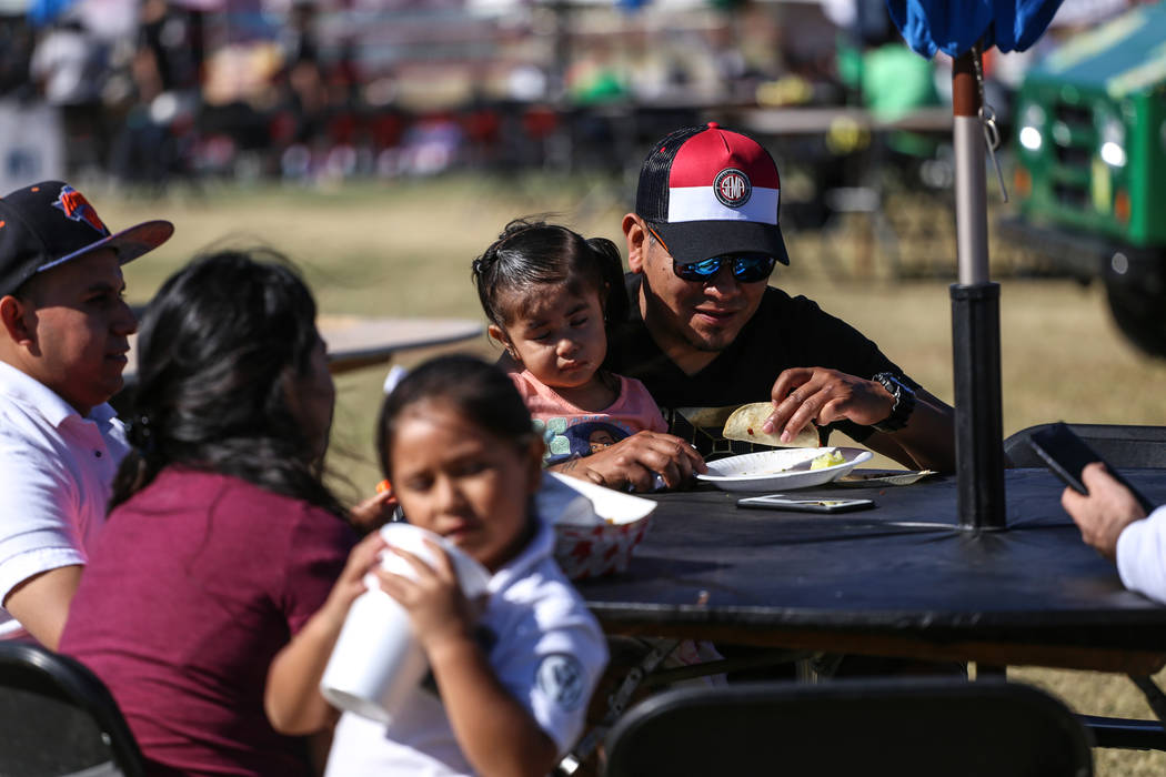 Cesar Gutierrez, 45, right, eats tacos as his daughter Stefania, 2, both of Las Vegas, sits on his lap at the Original LV Project Taco festival in North Las Vegas, Saturday, Nov. 4, 2017. Joel Ang ...