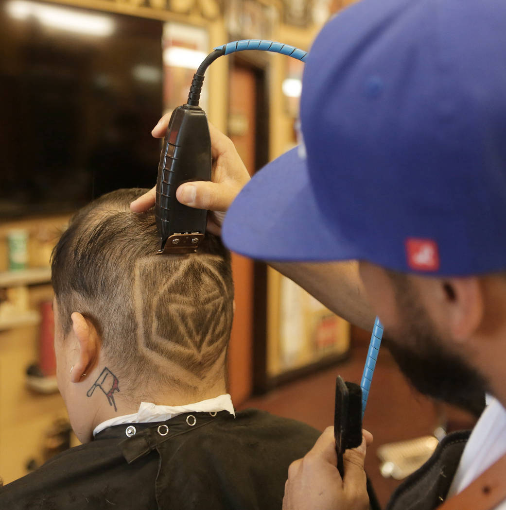 Fernando Guzmán, a la izquierda, de Las Vegas recibe un logo de los Golden Knights afeitado en la parte posterior de su cabeza por Moisés "Moy The Barber" Álvarez, propietario de Goodtimes Barb ...