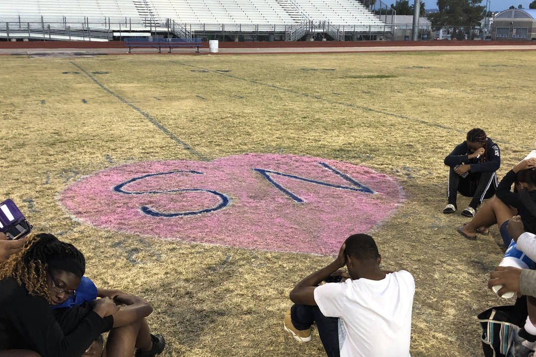 Personas se sientan y lloran alrededor de un corazón con las iniciales de Susan Nash, pintadas en medio del campo de fútbol de Desert Pines High School, el 24 de octubre de 2018. La escuela real ...
