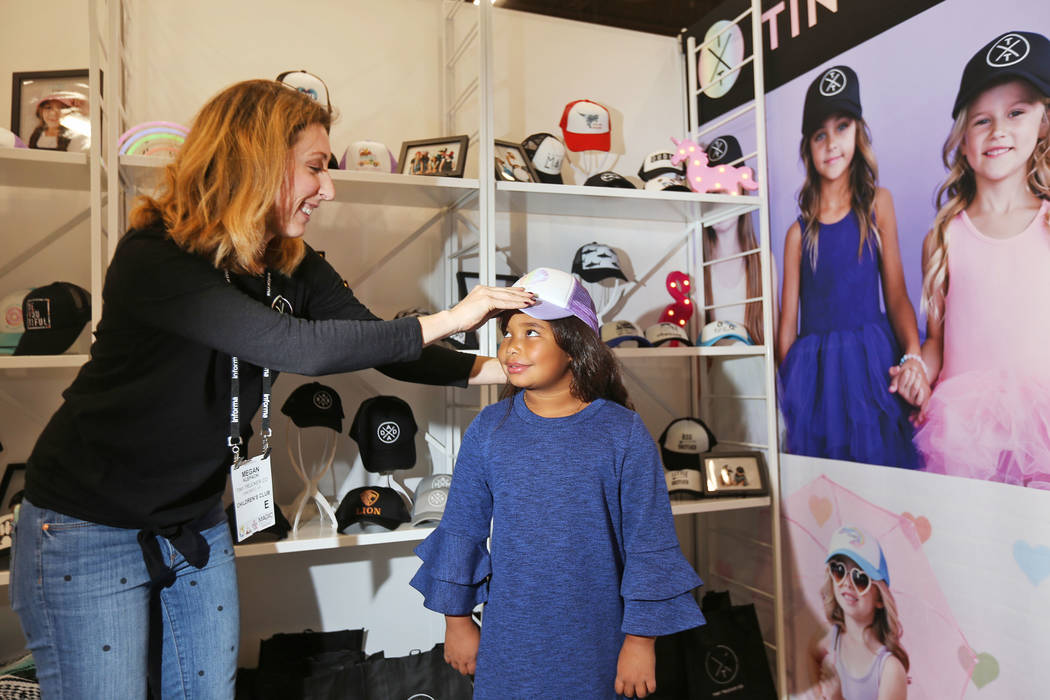 La directora de ventas Megan Klepacki coloca un sombrero de camionero en Destiny Klatt, de 9 años, en el stand de Tiny Trucker Co. en la feria de moda MAGIC en el Mandalay Bay Convention Center e ...