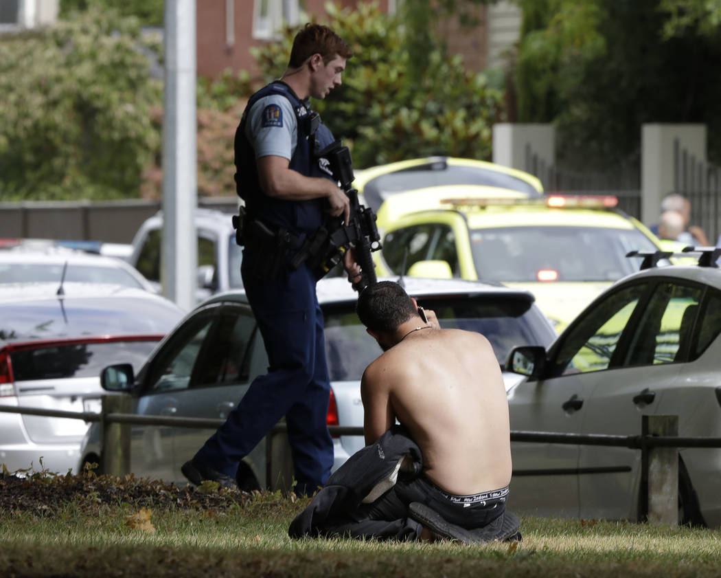 Un hombre descansa en el suelo mientras habla por su teléfono móvil al otro lado de la carretera de la mezquita en el centro de Christchurch, Nueva Zelanda, viernes 15 de marzo de 2019. (AP Phot ...