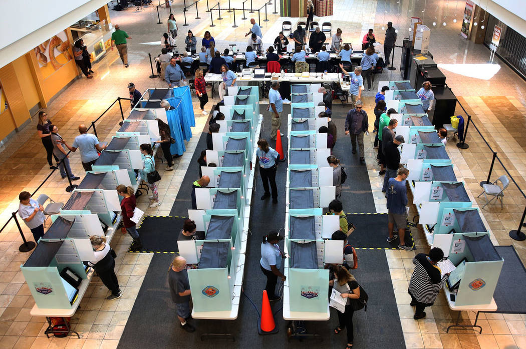 Los votantes depositan sus boletas electorales cuando otros se registran en una mesa electoral ...