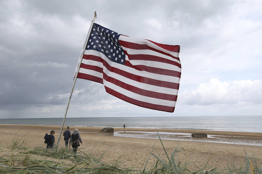 La gente camina por la playa de Omaha, Normandía, Francia, donde se planta una bandera estadou ...