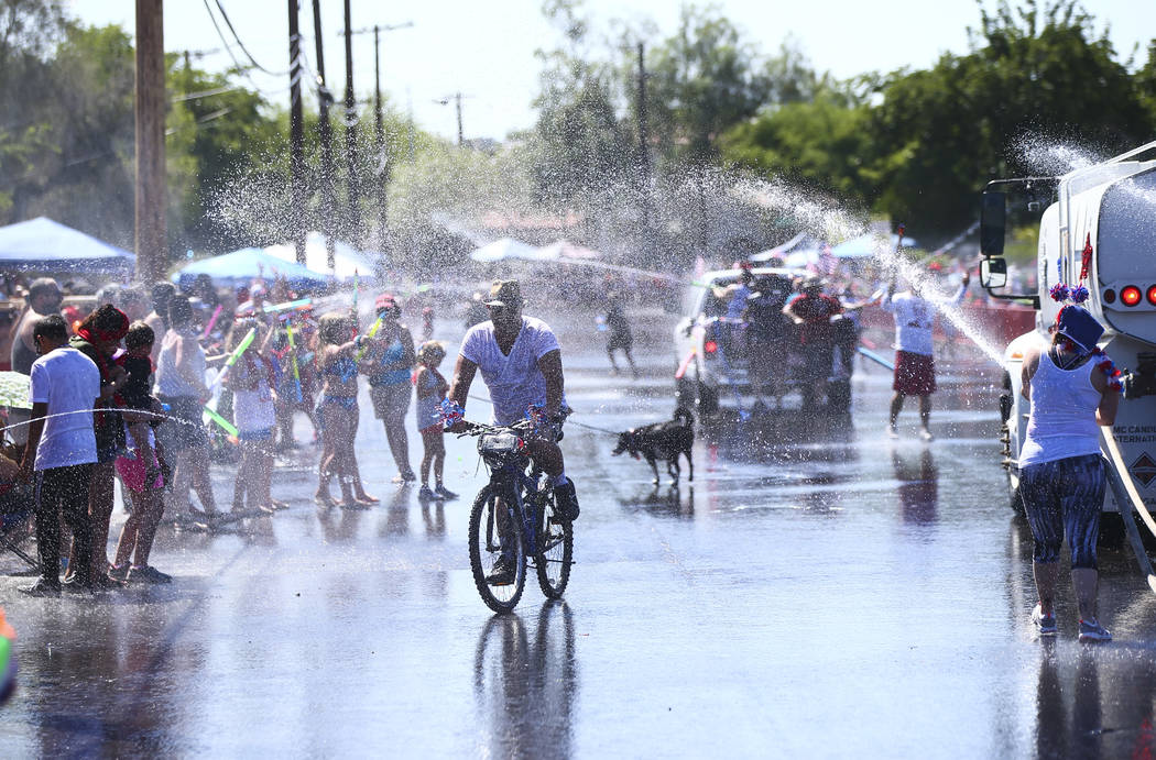 Un hombre monta su bicicleta mientras los espectadores y los participantes del desfile se rocí ...