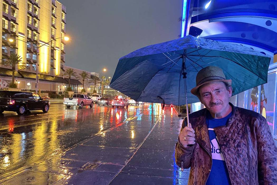 Jimmy James usa un paraguas para protegerse de la lluvia mientras espera un autobús alrededor ...