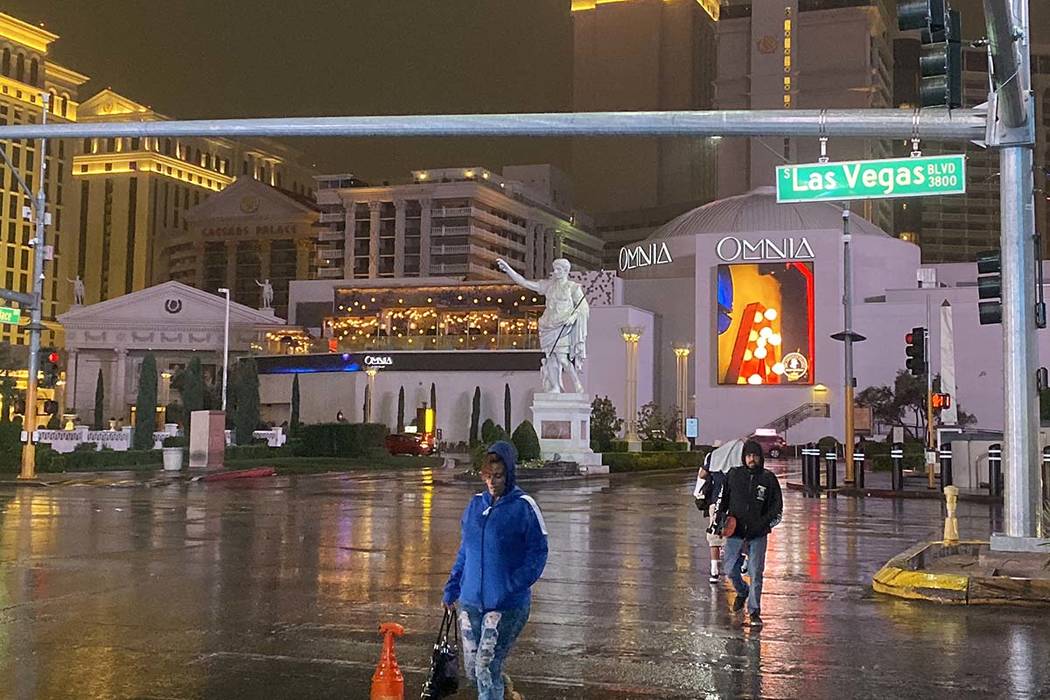 Peatones cruzan el Strip de Las Vegas cerca del Caesars Palace bajo la lluvia el miércoles, 20 ...