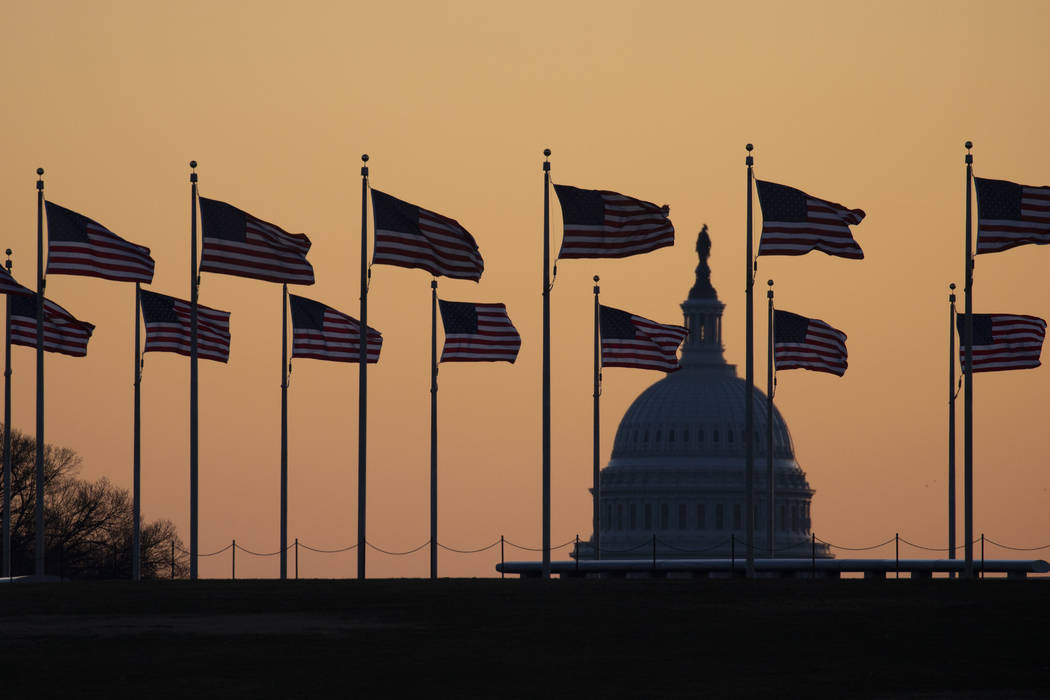 Banderas estadounidenses ondean al viento alrededor del Monumento a Washington con el Capitolio ...