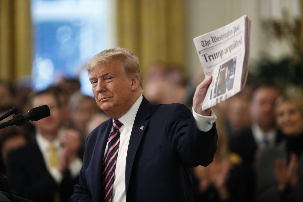 El presidente Donald Trump sostiene un periódico con el titular que dice "Trump absuelto" mien ...