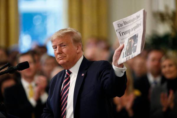 El presidente Donald Trump sostiene un periódico con el titular que dice "Trump absuelto" mien ...