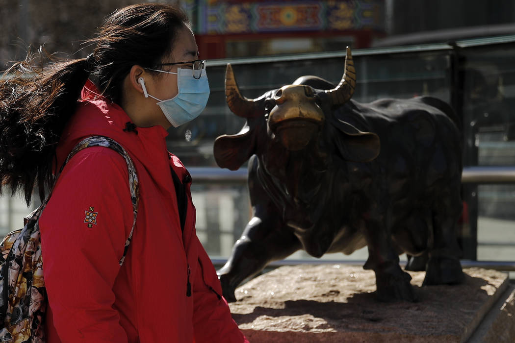 Una mujer con una mascarilla protectora camina por la estatua del toro, icono de las inversione ...