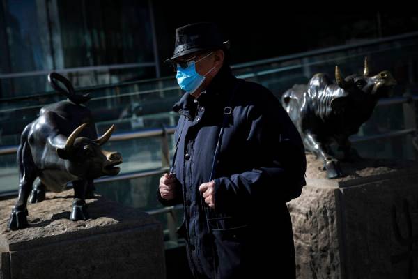 Un hombre con una mascarilla protectora camina por la estatua del toro, icono de las inversione ...
