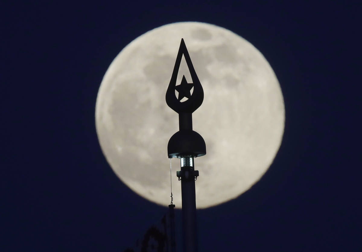 Una luna casi llena se levanta detrás de la cima del asta de la bandera en State Flag Square e ...