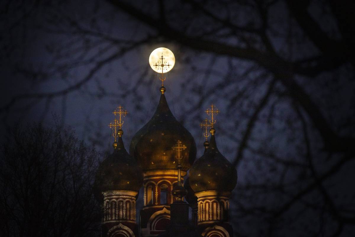 La superluna se eleva detrás de una cruz iluminada de una iglesia ortodoxa cristiana en Moscú ...