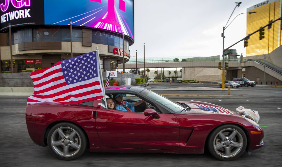 Un participante ondea una bandera estadounidense mientras los vehículos suben por el Strip de ...