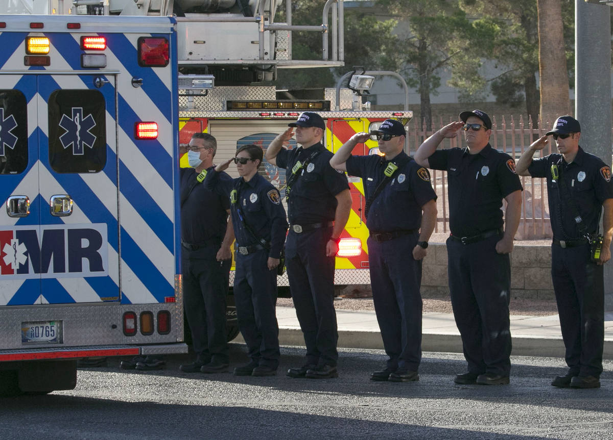 Bomberos del Condado Clark saludan durante una procesión mientras una ambulancia que lleva al ...
