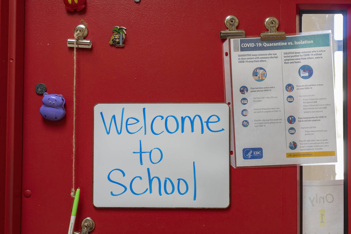 Un letrero da la bienvenida a los estudiantes a la escuela junto a una guía de COVID-19 en la ...