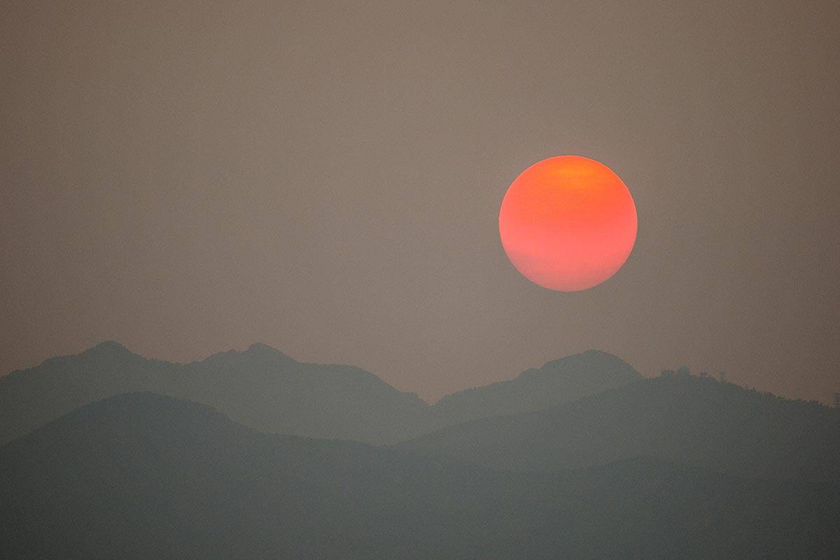 El sol, nublado por el humo de los incendios forestales en California, se pone detrás del áre ...
