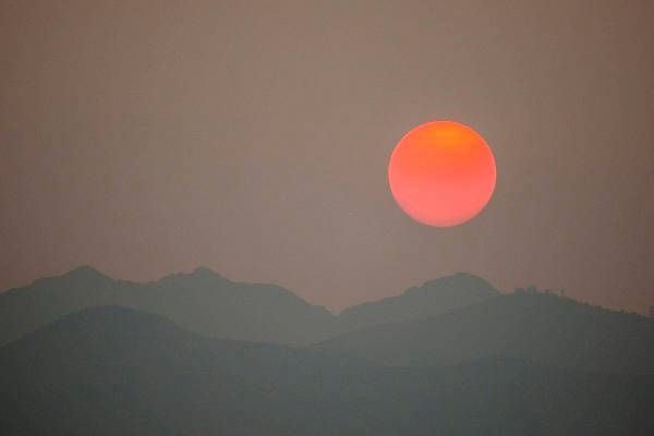 El sol, nublado por el humo de los incendios forestales en California, se pone detrás del áre ...