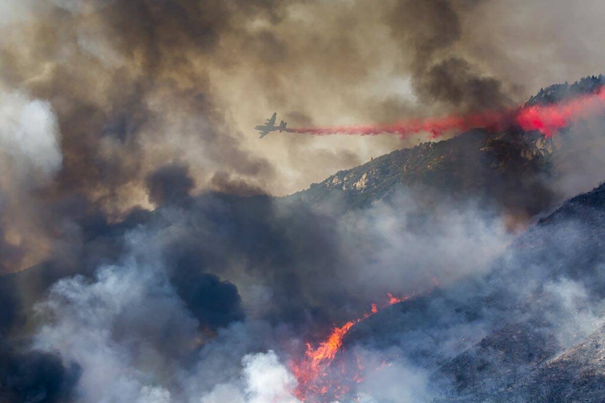 Un camión cisterna lanza un retardante en un incendio forestal que arde en una colina en Yucai ...