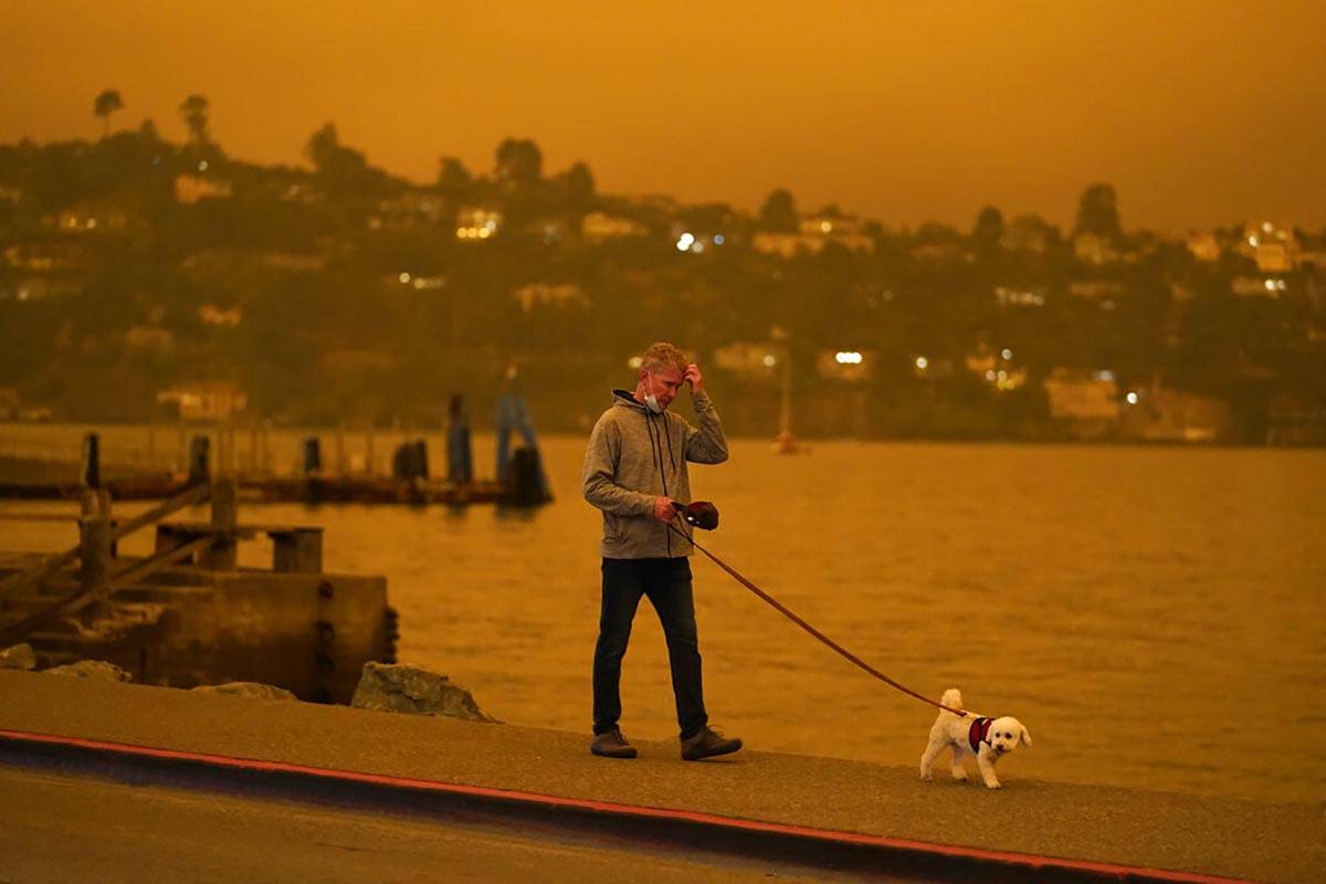 Un hombre pasea a su perro por la avenida Bridgeway mientras el humo de los incendios forestale ...