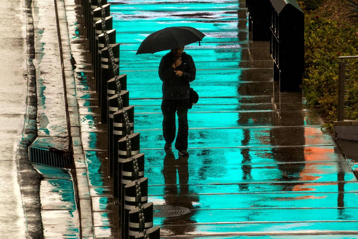 Un peatón es bañado por la luz azul de un letrero iluminado arriba mientras camina bajo la ll ...