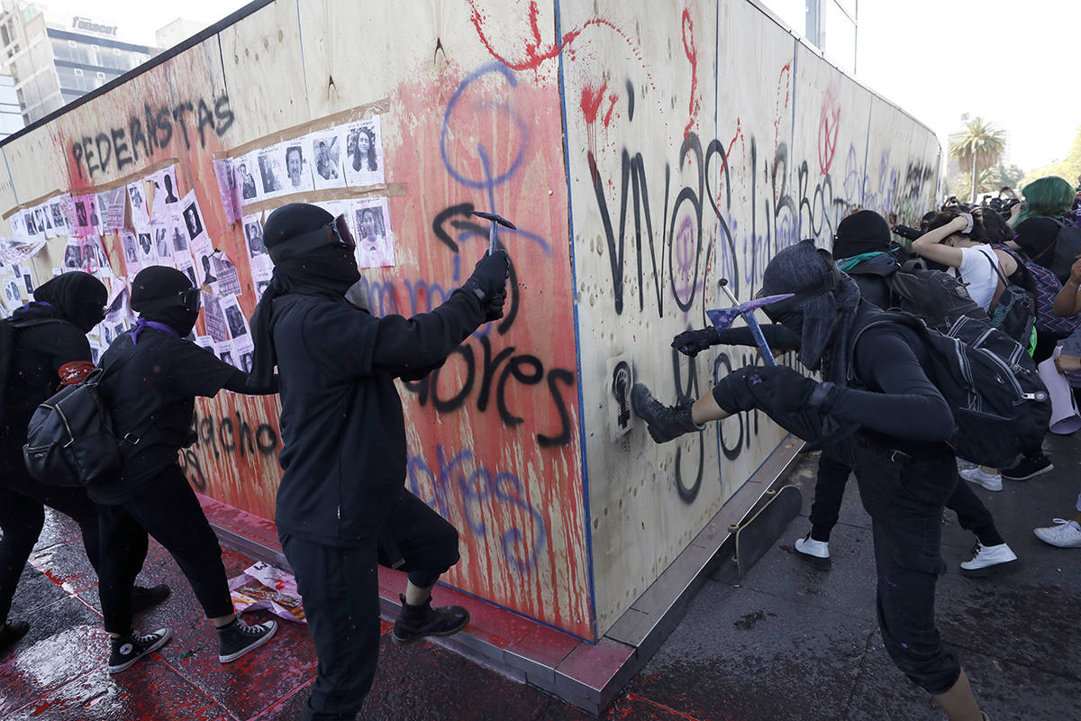 Mujeres atacan una pared de madera que protege el monumento a la Revolución de México durante ...