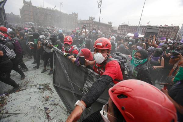 Paramédicos vestidos de rojo, intentan separar a manifestantes que chocan con la policía en u ...