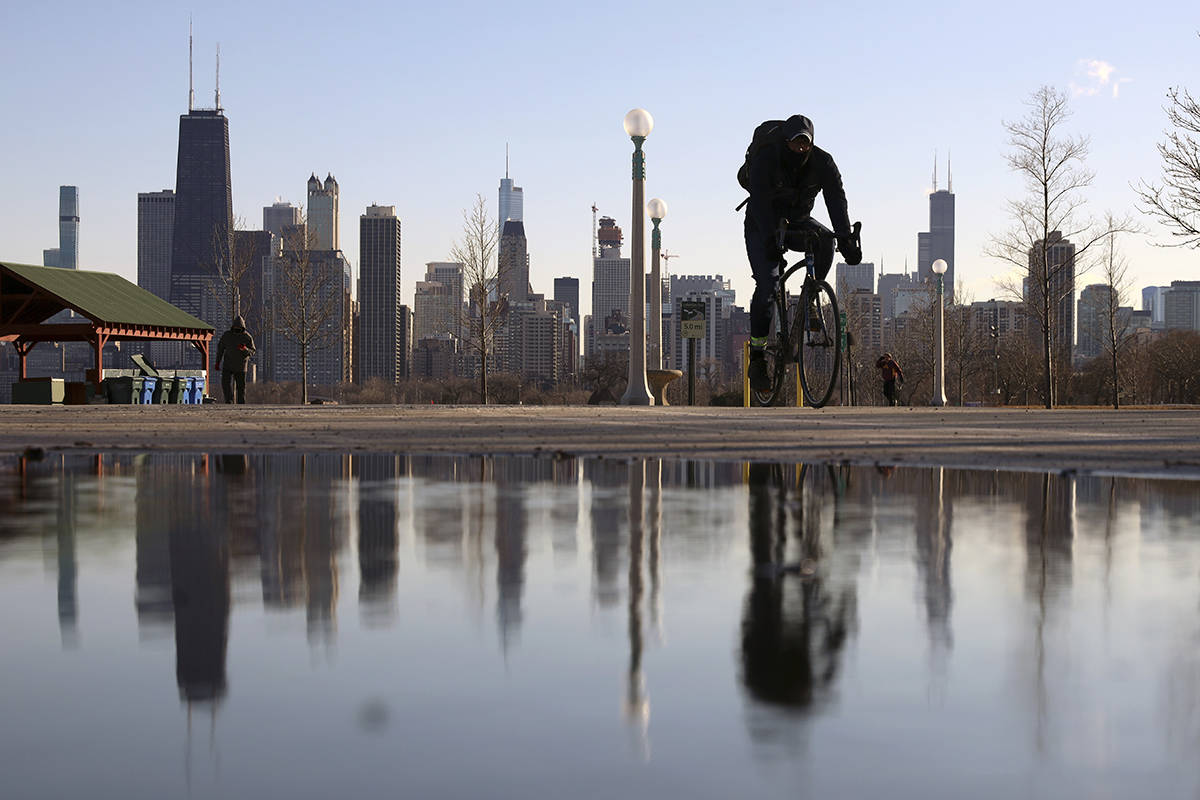 El horizonte de Chicago se refleja en el agua de la nieve descongelada mientras un ciclista pas ...
