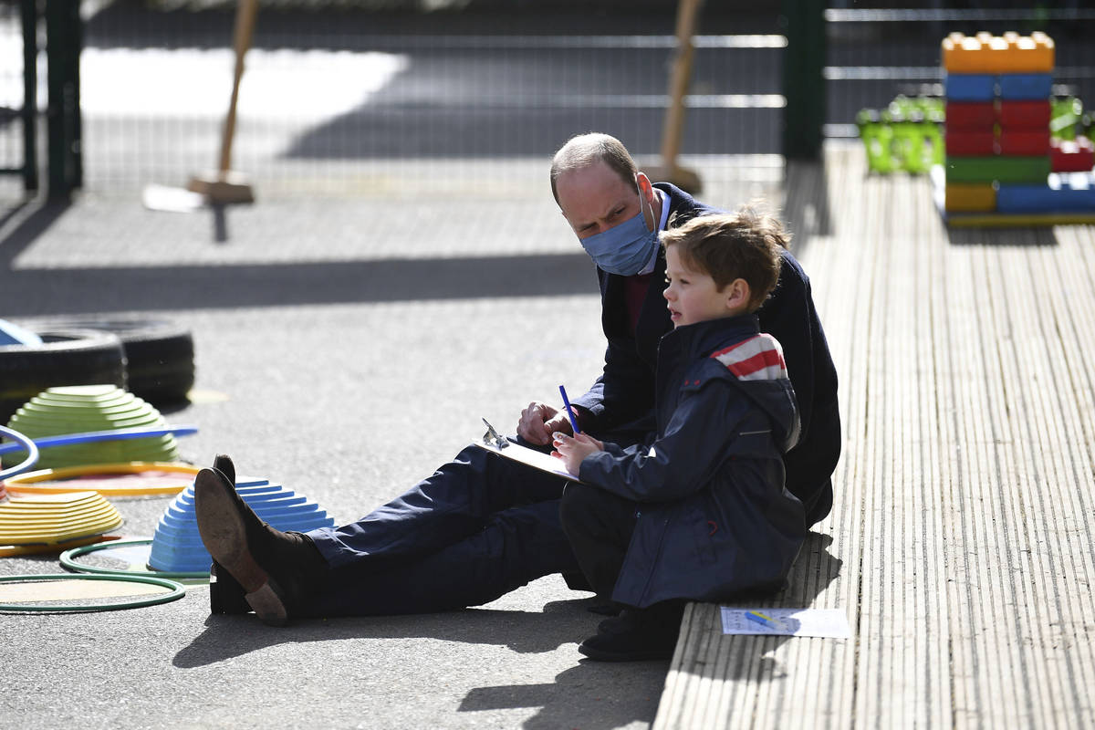 El príncipe británico William habla con un niño en el patio de recreo durante una visita con ...