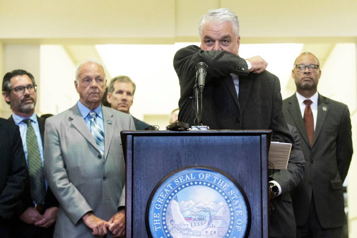 El gobernador Steve Sisolak demuestra la mejor manera de toser durante una conferencia de prens ...