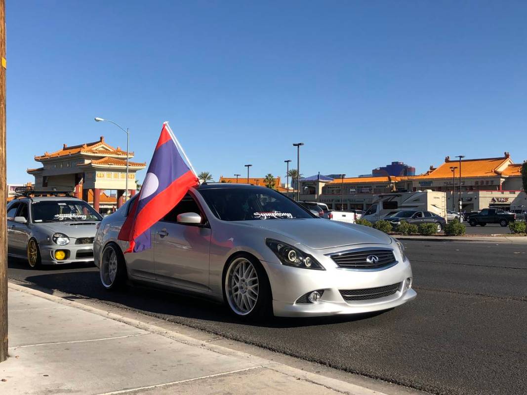 Un coche pasa por delante de los negocios de Chinatown mostrando la bandera de Laos durante el ...
