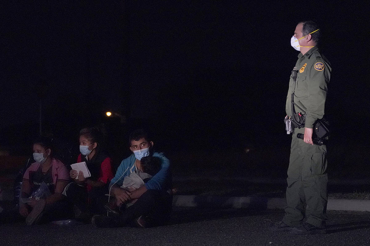 Un hombre migrante, en el centro, sostiene a un niño mientras mira a un agente de Aduanas y Pr ...
