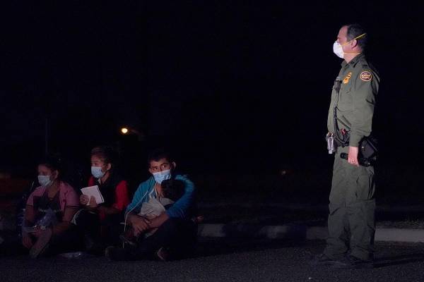 Un hombre migrante, en el centro, sostiene a un niño mientras mira a un agente de Aduanas y Pr ...