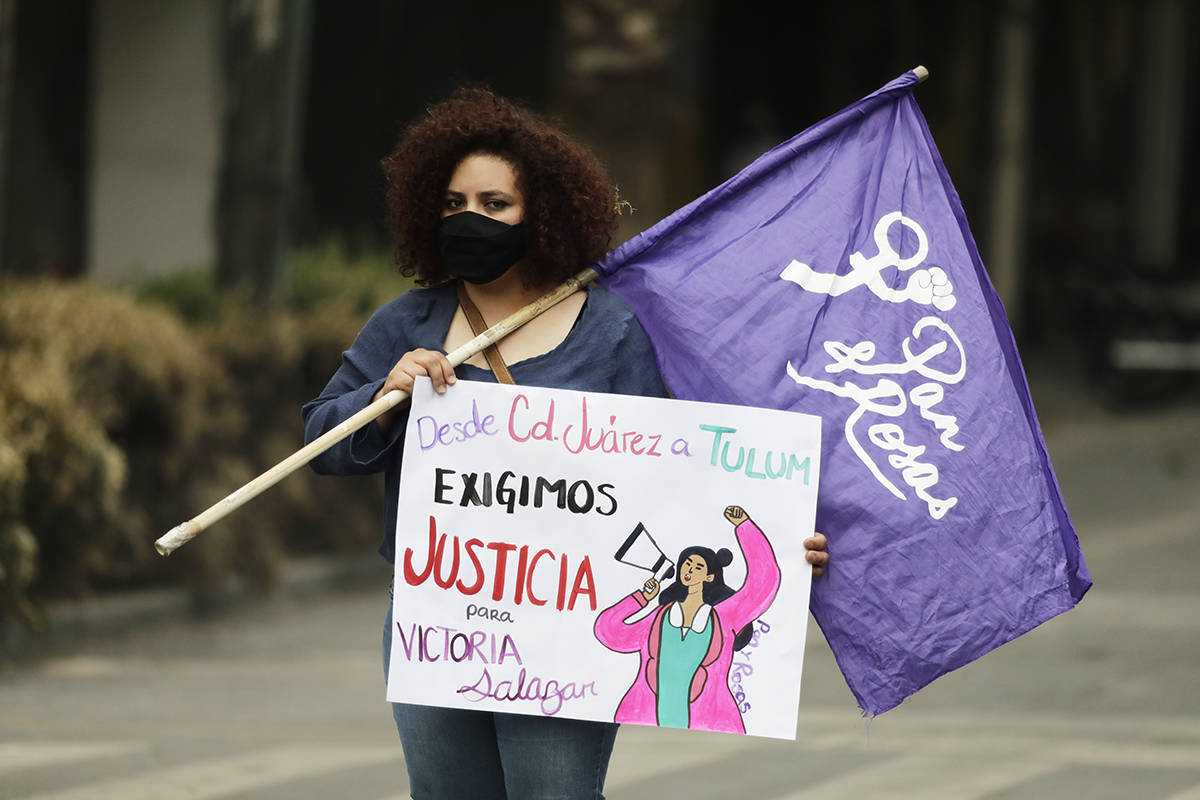 Una mujer sostiene una bandera feminista y un cartel que dice "De Ciudad Juárez a Tulum exigim ...