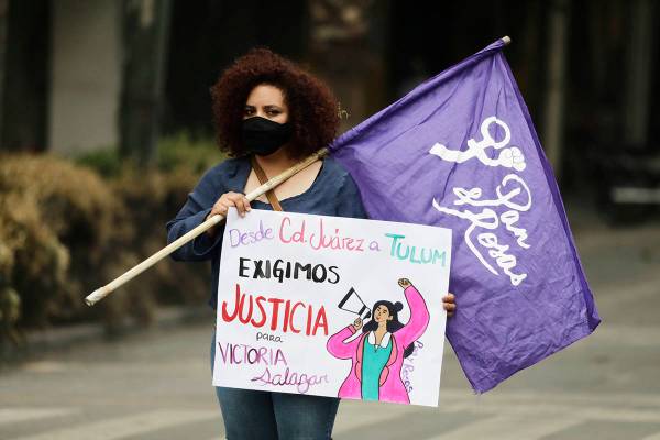Una mujer sostiene una bandera feminista y un cartel que dice "De Ciudad Juárez a Tulum exigim ...