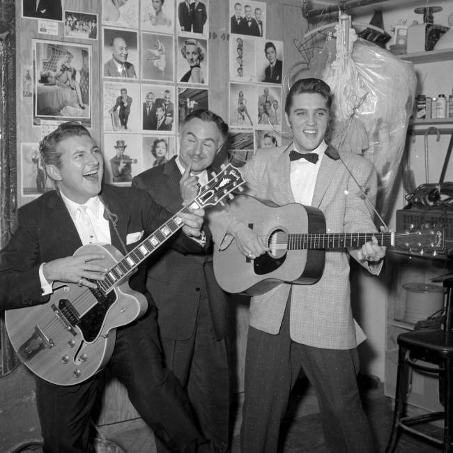 Liberace bromea con una guitarra mientras él y su hermano George Liberace visitan a Elvis Pres ...