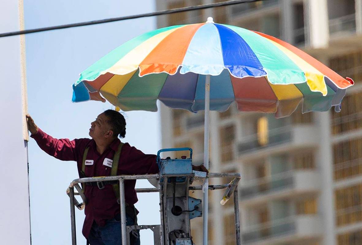 Un trabajador utiliza un paraguas gigante para protegerse del sol mientras trabaja en una estru ...