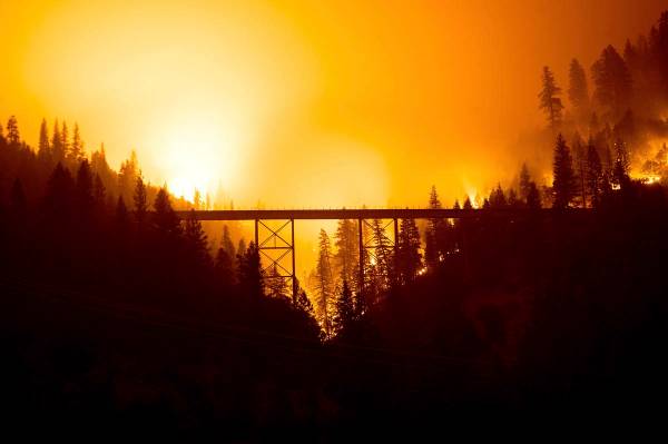Visto en una fotografía de larga exposición, el Dixie Fire arde detrás de un puente en el Co ...