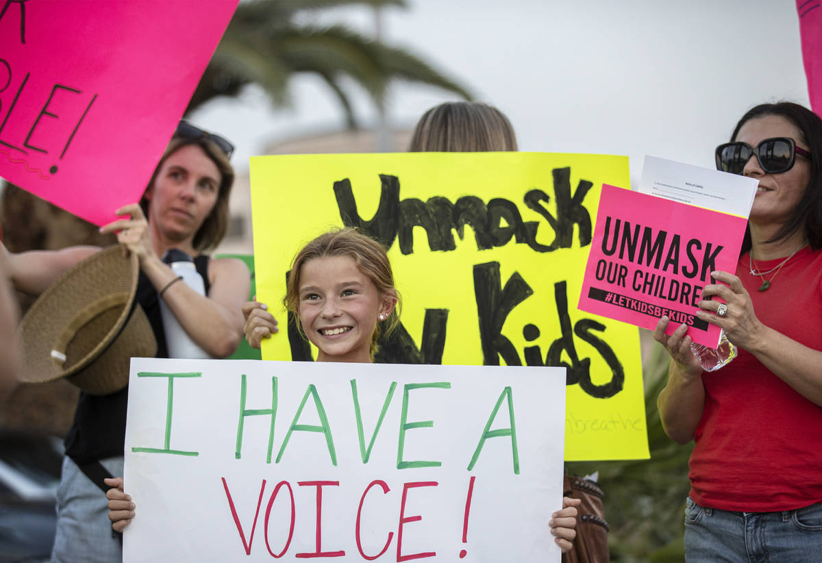 Ali Petersen, en medio, de 10 años, sostiene un cartel que se opone al mandato de cubrebocas p ...