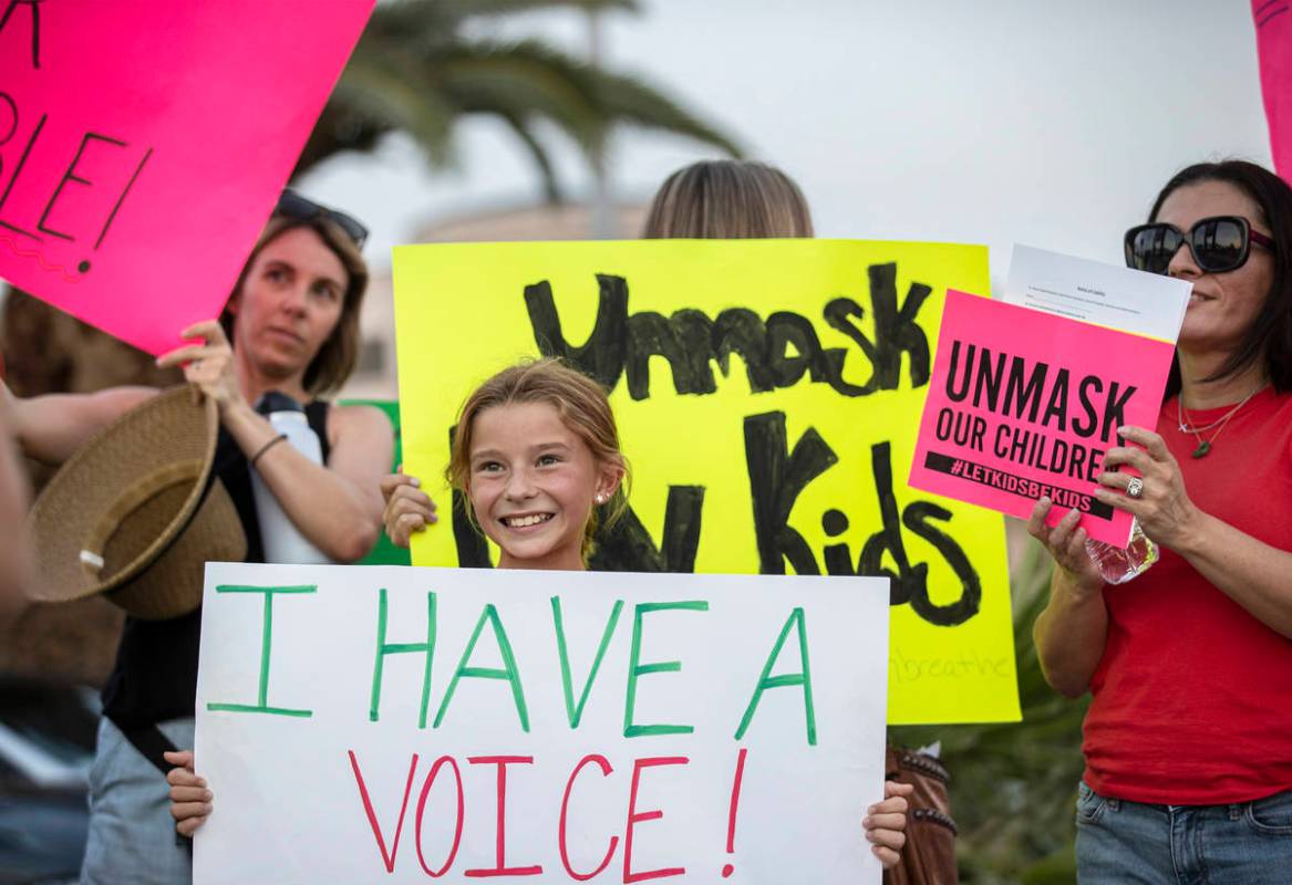 Ali Petersen, en medio, de 10 años, sostiene un cartel que se opone al mandato de cubrebocas p ...