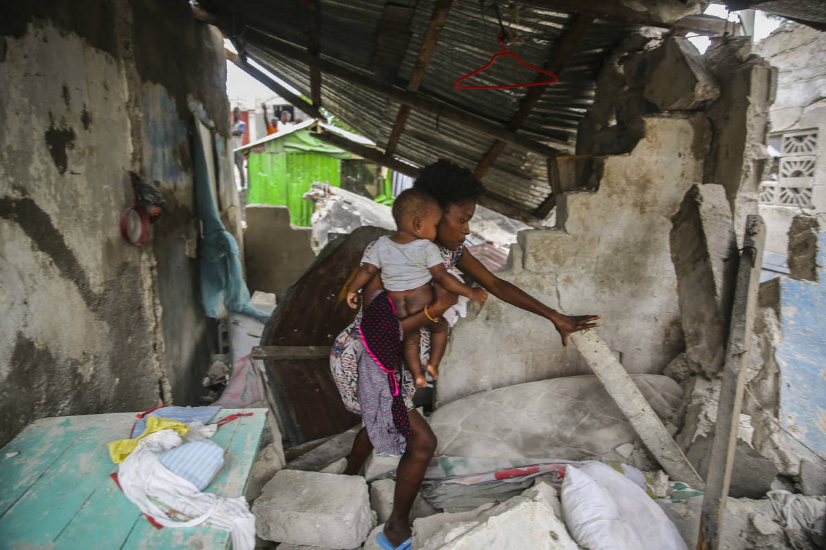 Una mujer carga a su hijo mientras camina entre los restos de su casa destruida por el terremot ...