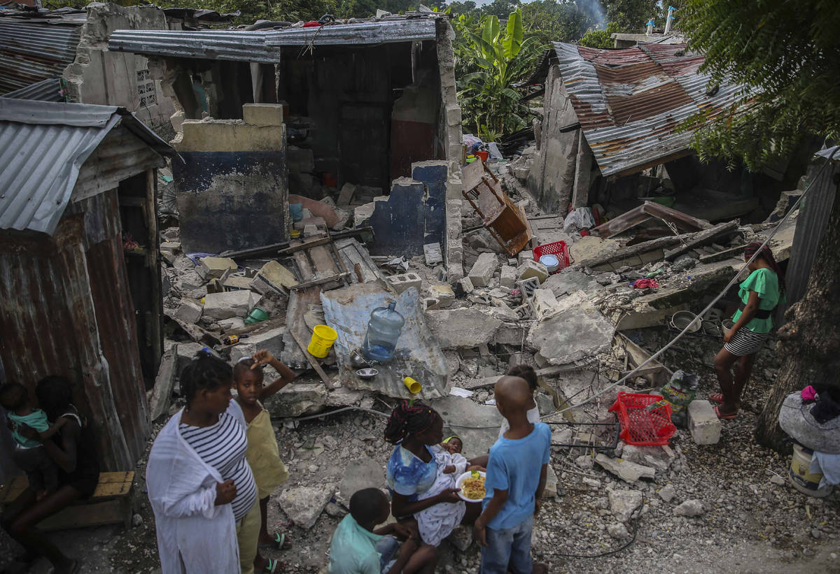 Una familia desayuna frente a las casas destruidas por el terremoto de 7.2 grados en Les Cayes, ...