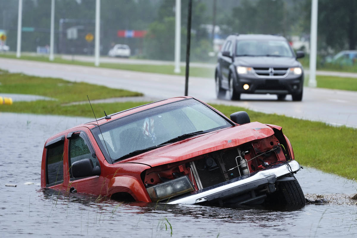 Un vehículo abandonado está medio sumergido en una zanja junto a una carretera casi inundada ...