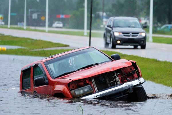 Un vehículo abandonado está medio sumergido en una zanja junto a una carretera casi inundada ...