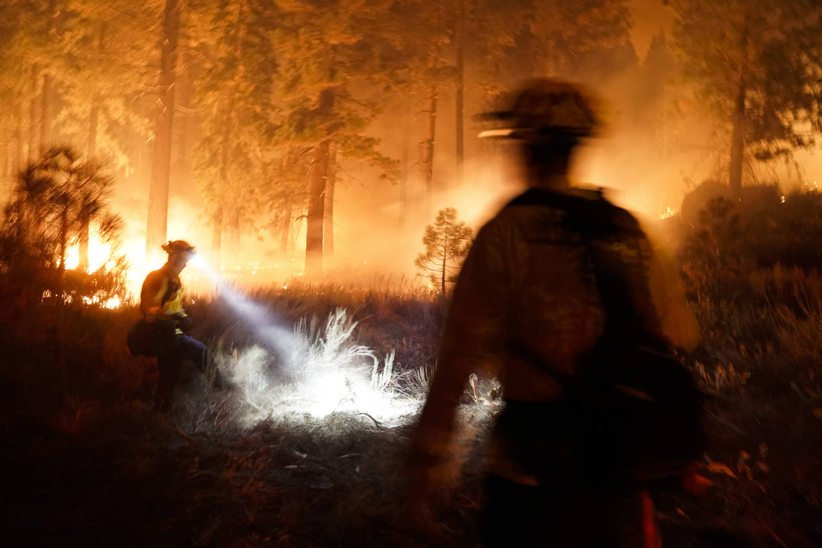 Dos bomberos crean un corte de combustible mientras el “Caldor Fire" arde cerca de las casas ...